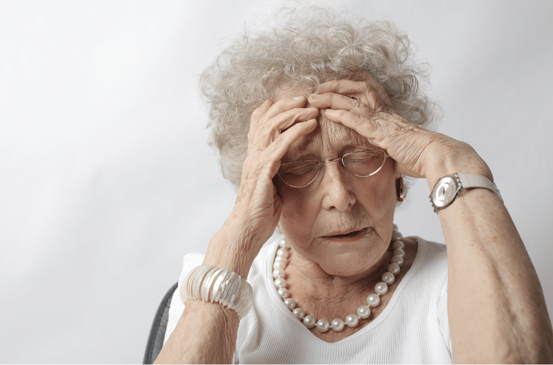 Mujer mayor preocupada con manos en la cabeza para representar el estrés en la cuidador de una persona con Alzheimer