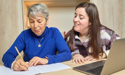 Actividades de estimulación cognitiva. Persona mayor escribiendo con ayuda de cuidadora.