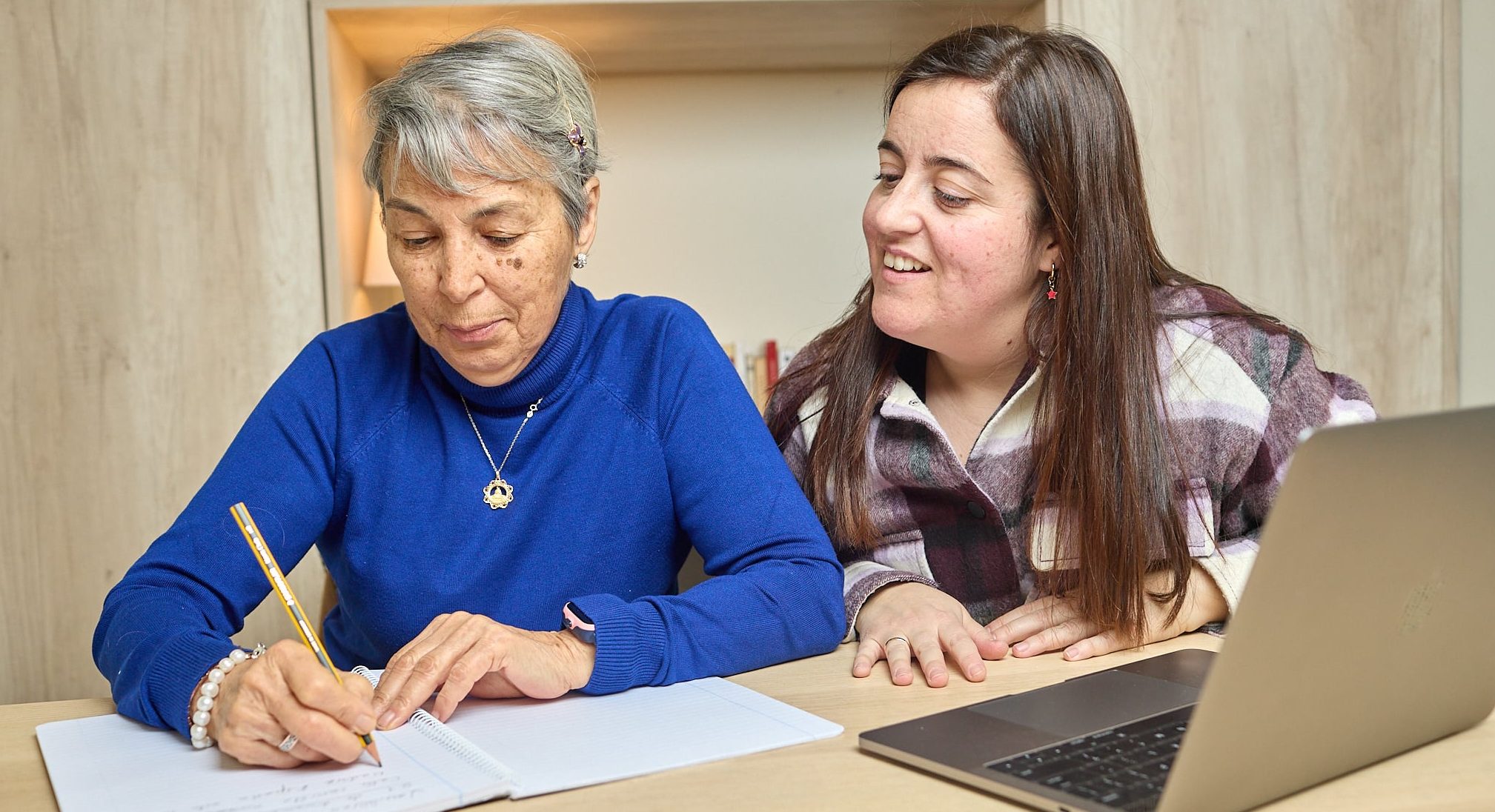 Actividades de estimulación cognitiva. Persona mayor escribiendo con ayuda de cuidadora.